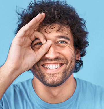 ein Mann mit dunklen Locken und Vollbart schaut lachend durch die Finger